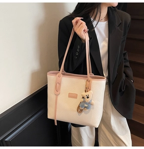 Close-up of white lychee leather tote bag with pink straps and cute bear charm