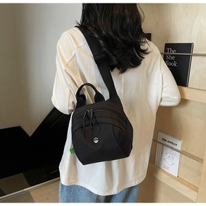 Rear view of a black nylon shell bag with multiple zippered pockets and wide shoulder strap