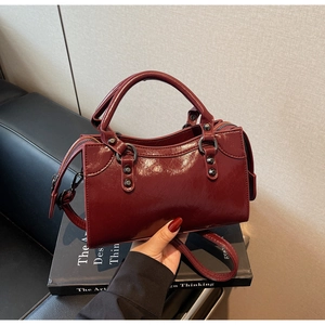 Detail einer dunkelroten Lackhandtasche mit schwarzen Metallringen und Nieten