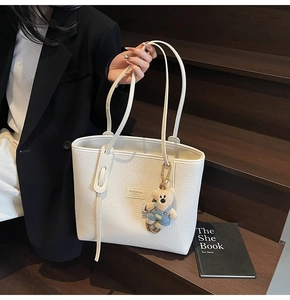 Detail of white lychee leather tote bag with brand logo and cute bear pendant charm