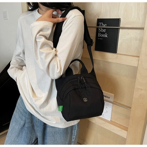 Detail of black nylon shell bag featuring dual zippers and adjustable shoulder strap