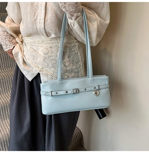 Detail view of light blue leather shoulder bag featuring a silver heart-shaped pendant detail