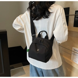 Detail of black nylon shell bag with metal logo and adjustable crossbody strap shown on model
