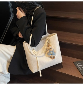 Detail of white textured tote bag with a cute plush bear charm on wooden stairs