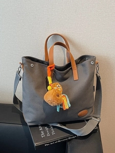 Gray canvas tote bag with leather straps and plush capybara charm shown from high angle