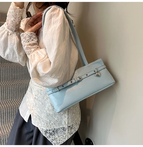 Detail of light blue underarm bag with silver heart pendant and textured leather