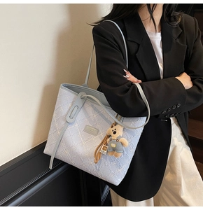 Dettaglio della borsa tote azzurra trapuntata con logo e ciondolo a forma di orso
