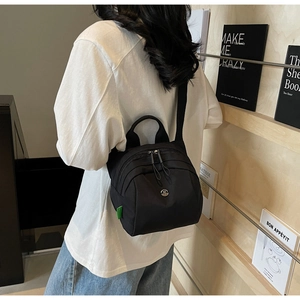 Detail of black nylon mini shell bag with dual zippers and green woven side label