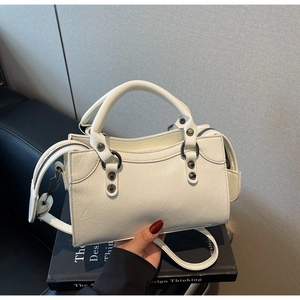 Detail einer weißen Handtasche aus Knautschlackleder mit Nieten auf Design-Büchern