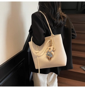 Detail of creamy white tote bag with pebble leather texture and a cute bear charm pendant