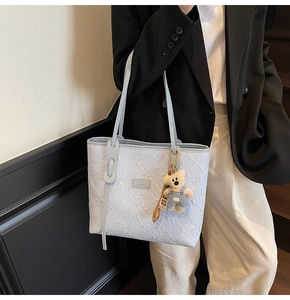 Dettaglio della borsa tote in jacquard azzurro con ciondolo a orsetto e logo