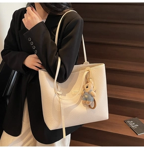 Close-up of beige lychee texture tote bag with a cute bear pendant on wooden stairs