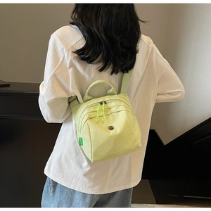 Detail of light green canvas mini shell bag showing dual zippers and top handle