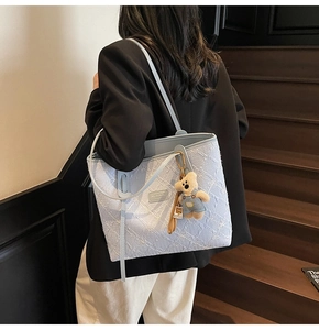 Dettaglio della borsa tote azzurra testurizzata con ciondolo a orsetto su scale in legno