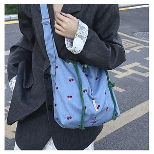 Detail of blue bucket bag with red cherry embroidery and green drawstring closure