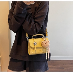 Détail d'un sac jaune avec boucle étoile argentée et pendentif ours en peluche