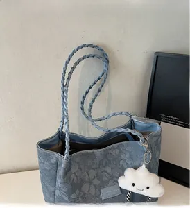 Detail of floral denim tote bag featuring braided handles and cloud plush charm