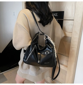 Close-up of black leather tote bag with silk scarf charm and zipper detail on shoulder