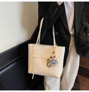 Detail of off-white lychee grain leather tote bag with a cute bear plush keychain