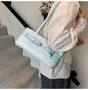 Close-up of light blue glossy underarm bag with a metal heart pendant and buckle detail
