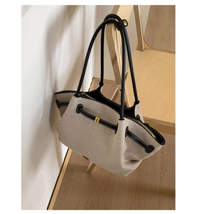 Detail of beige woven tote bag with black leather trim hanging on wooden chair back