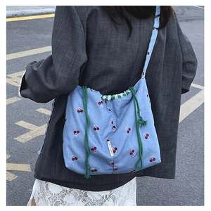 Detail of light blue canvas bucket bag featuring cherry patterns and green drawstring straps
