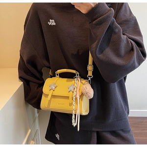 Detail of yellow leather mini bag with silver stars, fringe, and plush pompom charm