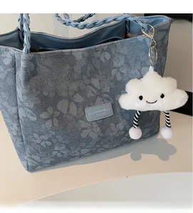 Close-up of blue floral denim tote bag with woven handles and white plush cloud charm
