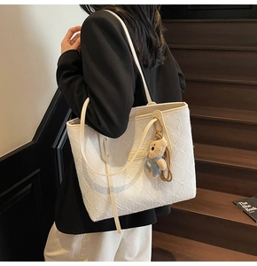 Dettaglio della borsa tote jacquard bianca con ciondolo a orsetto indossata a spalla