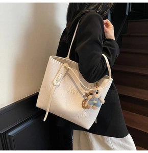 Detailed shoulder view of a cream leather tote bag with lychee texture and bear pendant