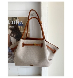 Detalle de costuras de lona y cuero marrón en el bolso tote con un logo dorado de marca