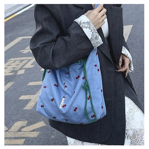 Detail of blue denim canvas bucket bag with cherry embroidery and green rope handles