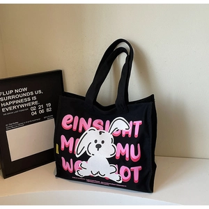 Detail of black canvas tote bag featuring white cartoon rabbit and pink lettering