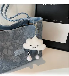 Close-up of white plush cloud pendant with smiley face on a floral denim tote bag
