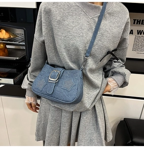 Detail of blue denim crossbody bag with silver metal buckles and decorative star rivets