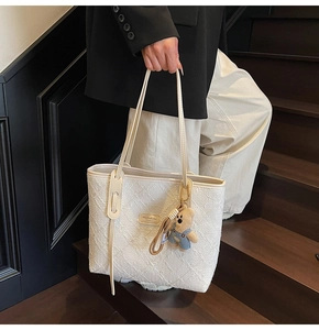 Dettaglio della borsa tote intrecciata crema con etichetta e ciondolo a orsetto
