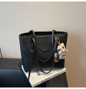 Detail of black pebbled leather tote bag with brand logo and cute plush bear charm