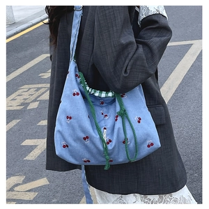 Detail of light blue canvas bucket bag with cherry embroidery and green drawstring closure