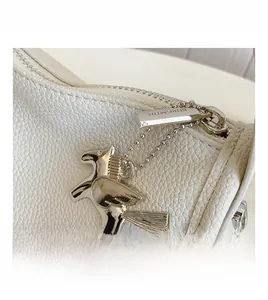 Macro shot of white pebble grain leather with a silver horse charm and branded metal zipper