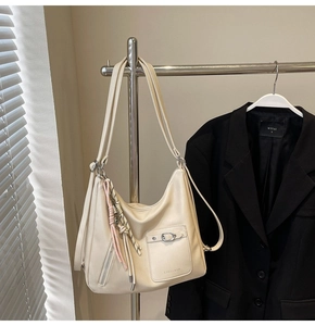 Close-up of cream PU leather tote showing functional metal buckle pockets and woven pendant