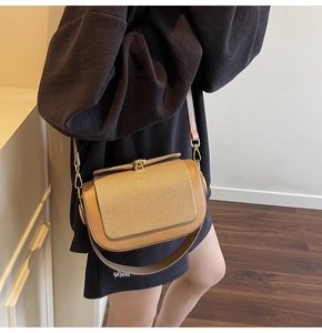 Detail of camel brown crossbody bag with woven texture flap and gold metal buckle on a model