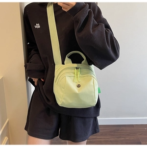 Detail of lime green canvas shell bag showing zippers and crossbody strap on model