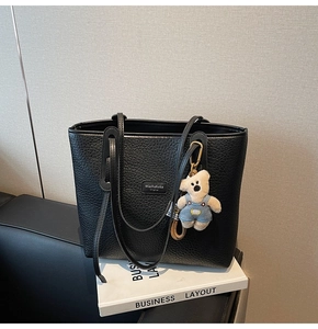 Detail of black pebbled leather tote bag with a cute plush bear charm and leather logo tag