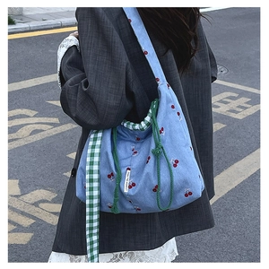 Detail of blue canvas bucket bag with cherry pattern and green checkered shoulder strap