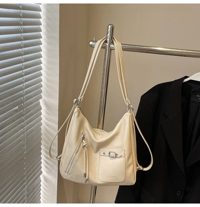 Detail of cream hobo bag showing front zipper tassel and buckled pocket with logo