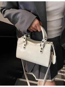 Weiße gefaltete Umhängetasche mit Metallnieten und Herzanhänger, von Model gehalten