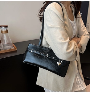 Detail of black glossy shoulder bag with buckle strap and silver heart pendant charm