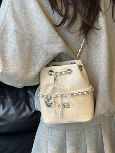 Creamy white drawstring bucket bag with chain and pearl bow charm worn on shoulder
