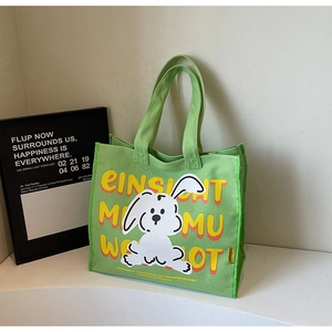 Detail of light green canvas tote bag showing cute cartoon bunny and yellow letter print