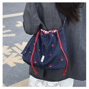 Detail of blue denim bucket bag with red cherry embroidery and cotton drawstring